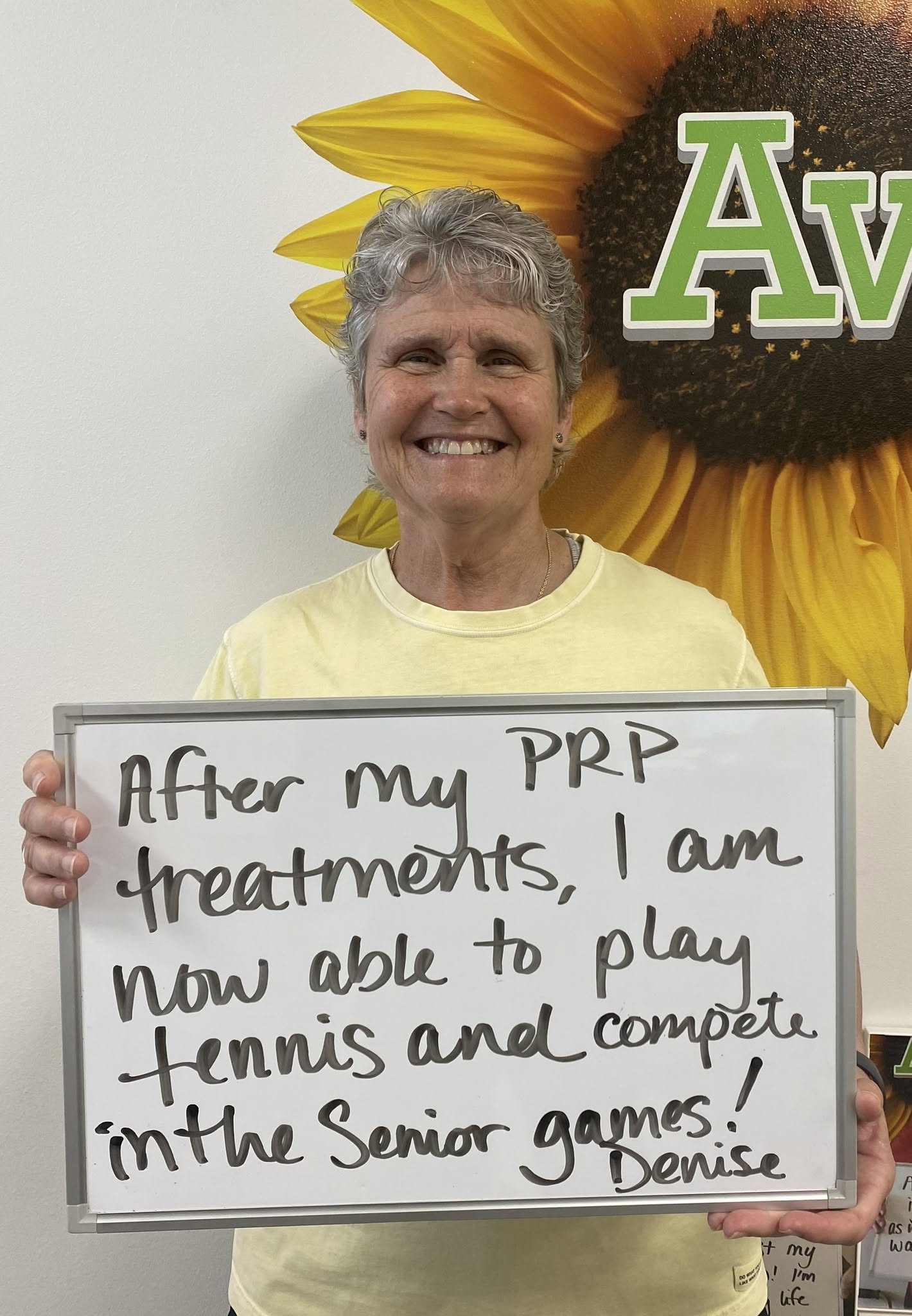 Denise, a Vitality Healing Center patient, holding a handwritten whiteboard about playing tennis and competing in the Senior Games after PRP treatments.