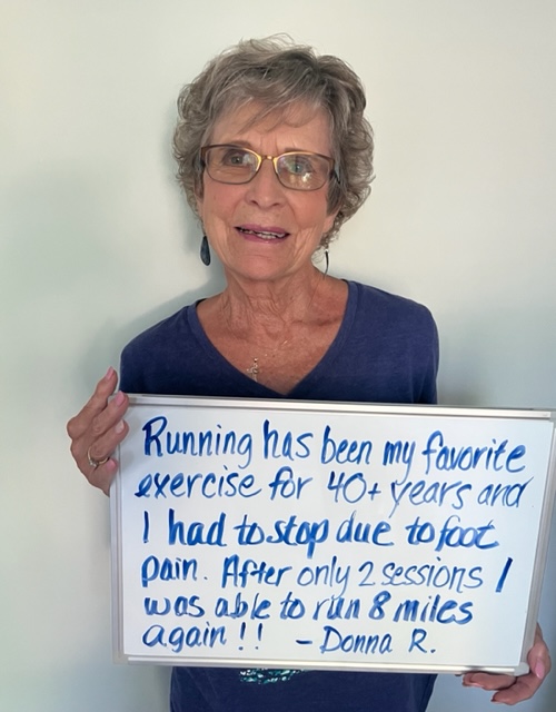 Donna R., a Vitality Healing Center patient, holding a handwritten whiteboard describing running 8 miles again after two treatment sessions.