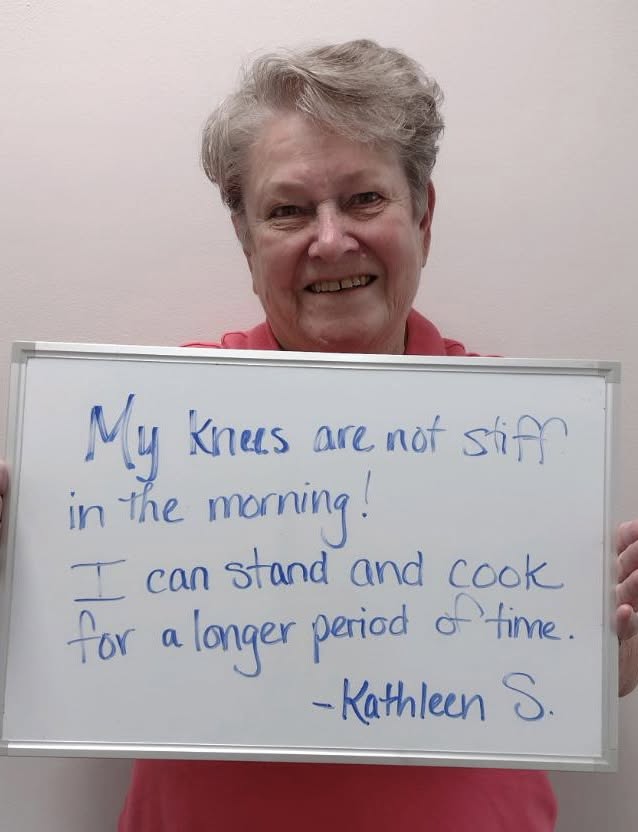 Kathleen S., a Vitality Healing Center patient, holding a handwritten whiteboard about standing and cooking for a longer period of time.