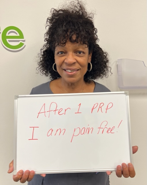 Mattie, a Vitality Healing Center patient, holding a handwritten whiteboard that reads: After 1 PRP I am pain free.