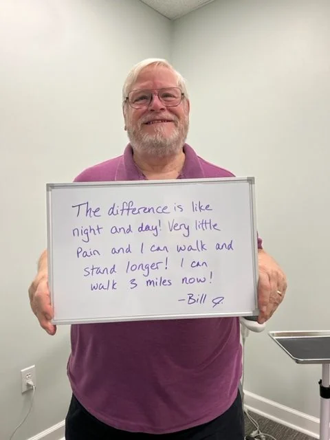 Bill S., a Vitality Healing Center knee patient, holding a handwritten whiteboard that reads: The difference is like night and day. Very little pain and I can walk and stand longer. I can walk 3 miles now.