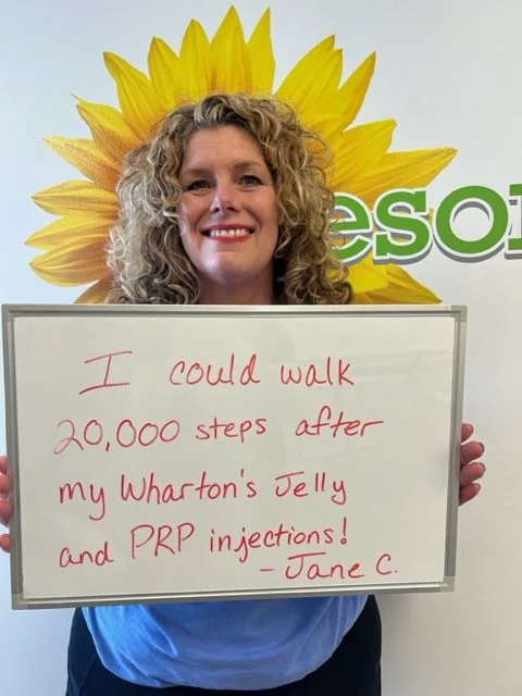 Jane C., a Vitality Healing Center patient, holding a handwritten whiteboard that reads: I could walk 20,000 steps after my Wharton's Jelly and PRP injections.