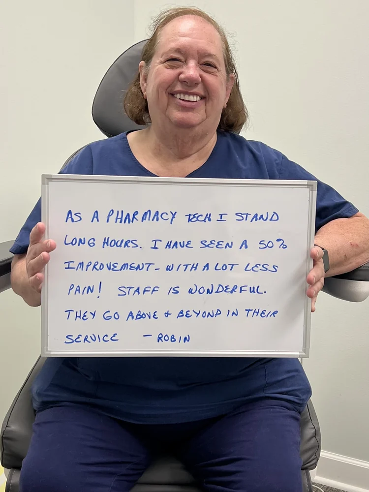 Robin B., a pharmacy technician and Vitality Healing Center patient, holding a handwritten whiteboard describing a 50 percent improvement in knee pain.